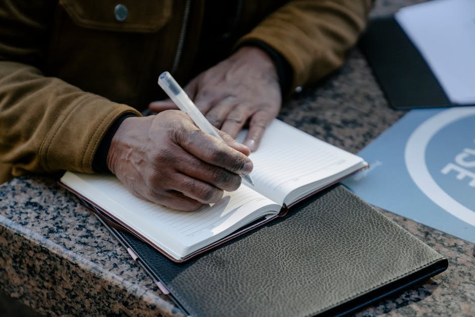 Person writing in a leather-bound journal on a wooden desk with morning coffee