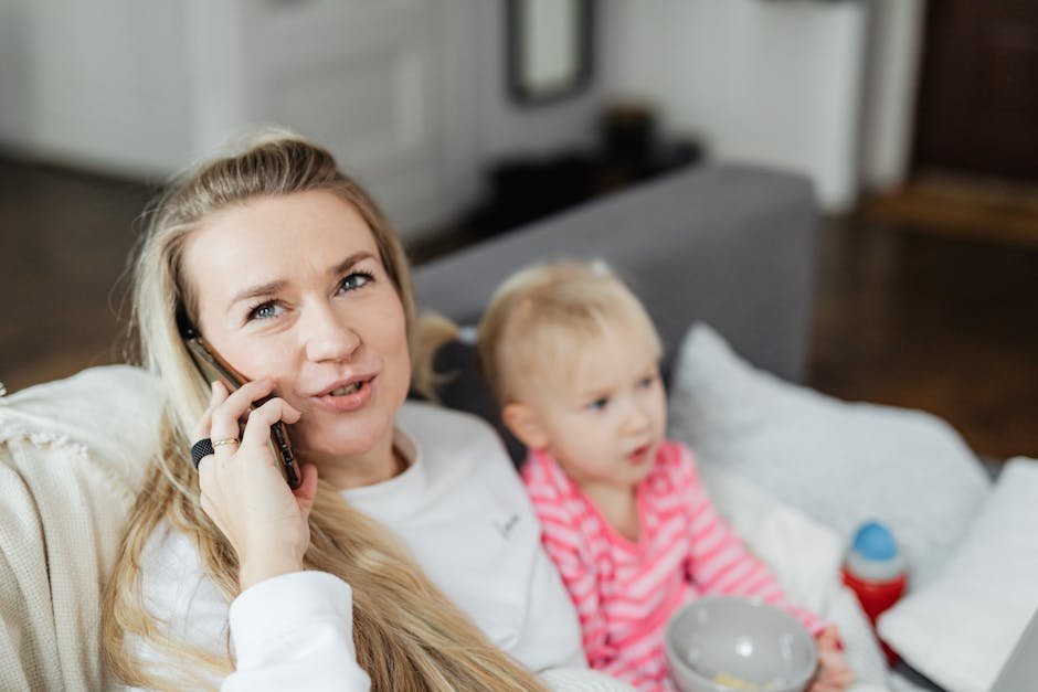 Mother on phone reviewing UnitedHealthcare insurance paperwork at a kitchen table while a teenager sits on the couch