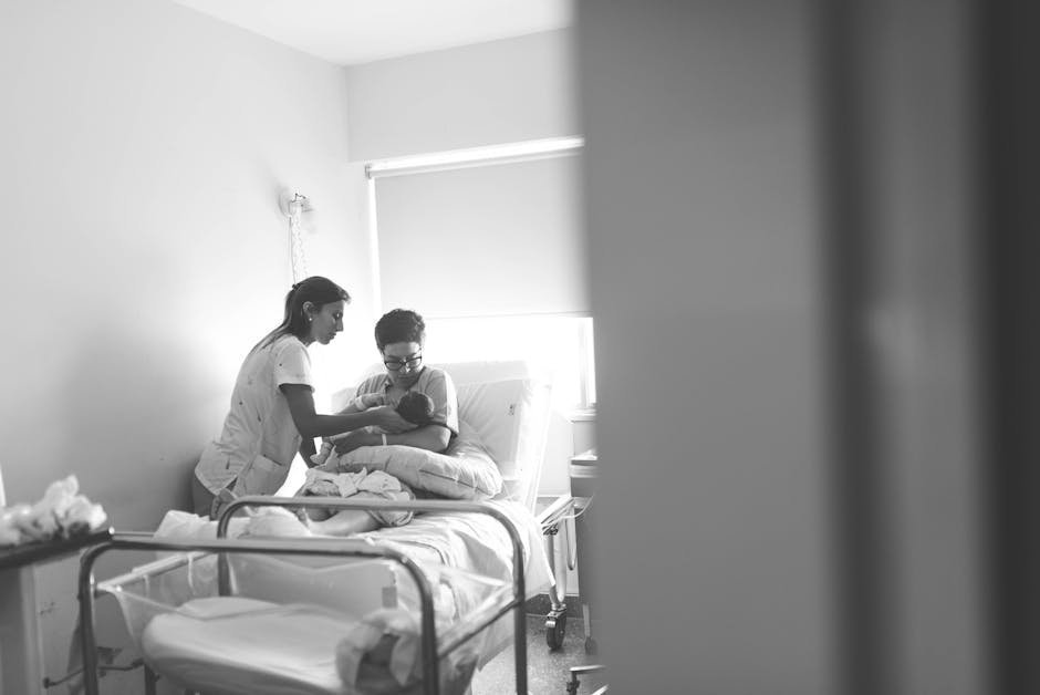 Mother holding her newborn in a calm hospital room with soft lighting and a crib